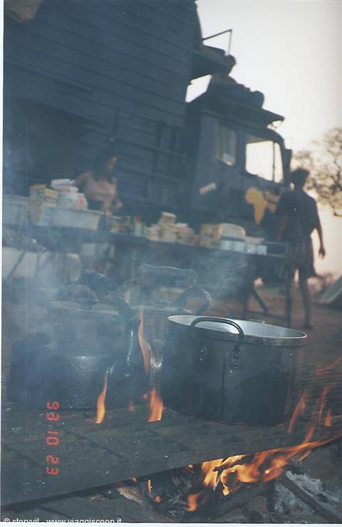 Pots over campfire flames and smoke, expedition truck in the background