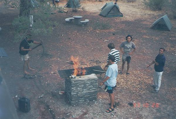 Campsite with tents, young people around a fire burning on a stone grill