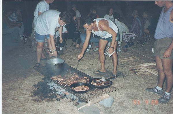 Two men cooking meat and sausages on the barbecue grill at night