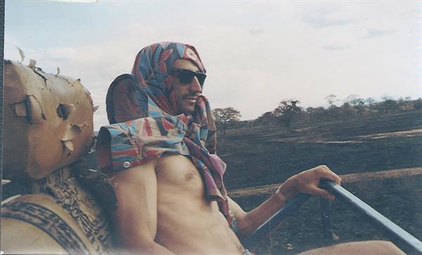 Shirtless man with headscarf and sunglasses on a safari truck in the savannah