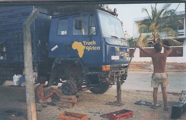 Mechanics repair a blue Leyland truck marked Truck Africa under palm trees
