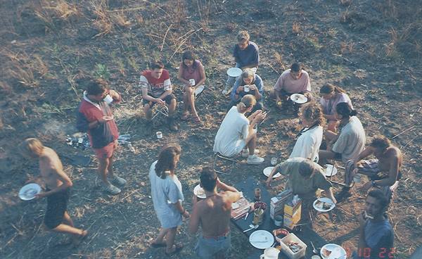 Group of young people standing around a table with plates on dry ground