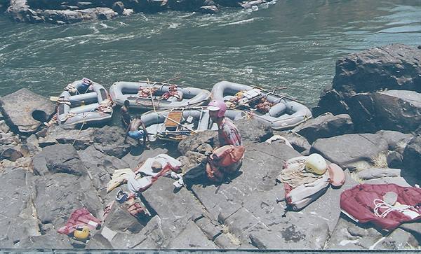 Rubber rafts on river rocks, people preparing with helmets and gear