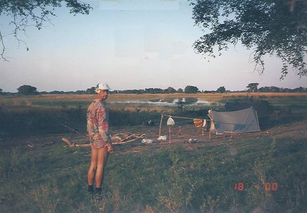 Camper beside a green tent on the bank of an African river