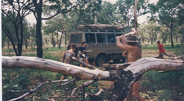 A man in a hat chops a fallen trunk beside the off-road vehicle in the bush