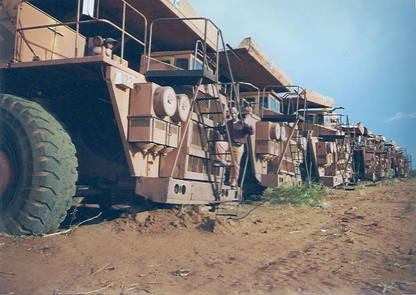 Woman standing on the ladder of a giant mining truck, red dirt ground