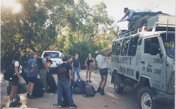 Travelers loading backpacks onto a Travelabout 4WD truck under sunny trees