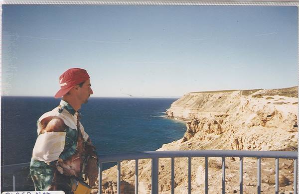 Man in red cap by a railing overlooking limestone cliffs and turquoise ocean