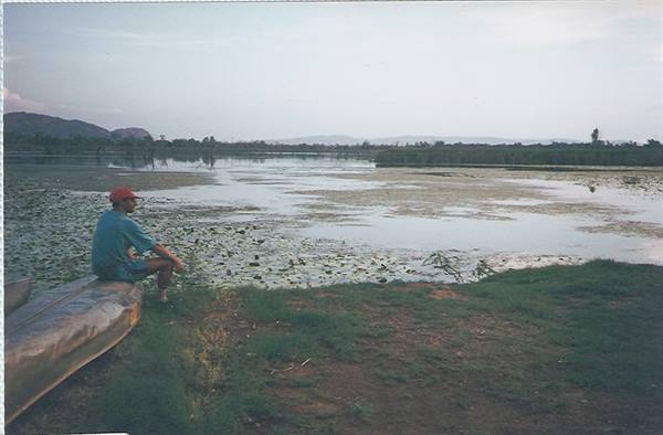 Man in red cap sitting on a canoe beside a lily-covered lake
