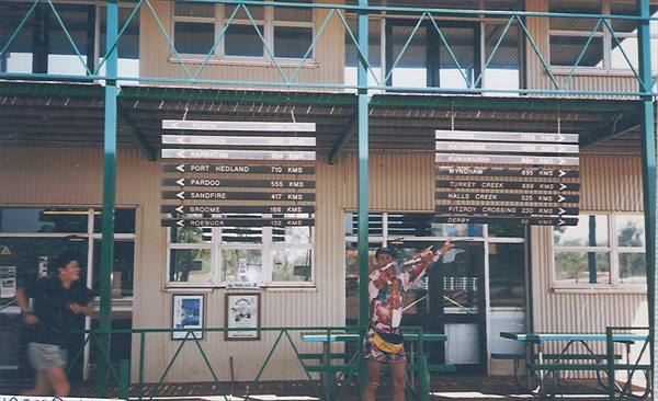 Traveler pointing at distance signs to Port Hedland and Broome outside a roadhouse