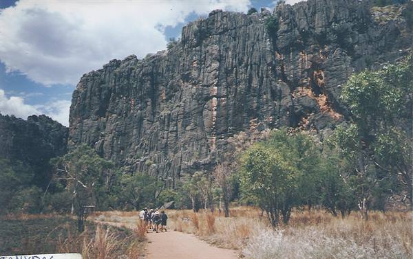 Tourists walk on sandy path beneath the tall rock cliffs of Windjana Gorge