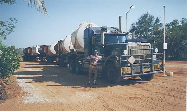 Tourist posing beside a road train tanker truck on a dirt road