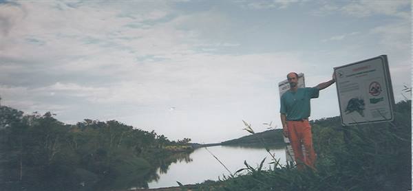 Man beside an information sign by the lake, tall grass, cloudy sky