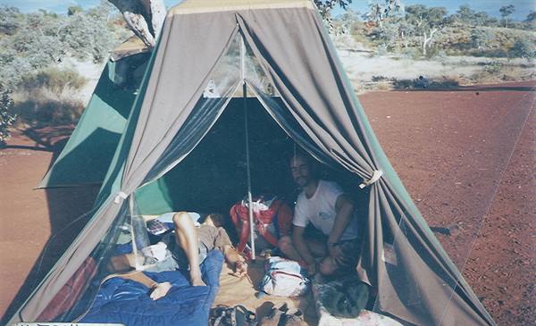 Two campers inside a green tent on the red dirt of the Australian outback