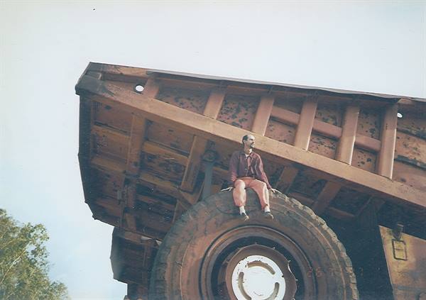 Guy sitting on the huge tire of a rusty mining dump truck
