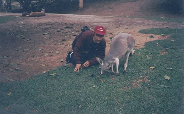Man crouching next to a grazing kangaroo on the grass