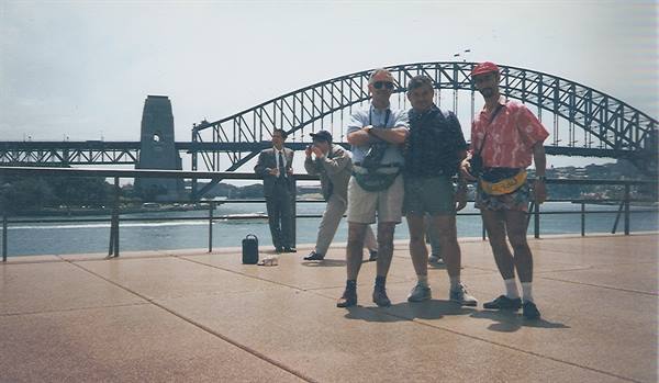 Three friends pose on the waterfront in front of the steel Sydney Harbour Bridge