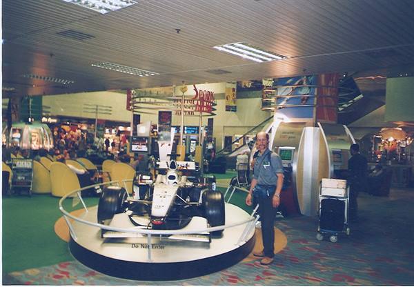Tourist posing next to a Formula 1 race car displayed at the airport