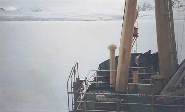 Ship surrounded by sea ice, onboard crane, snow-covered mountains behind