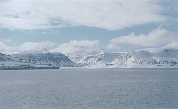 Frozen sea before snow-covered mountains under clouds, Svalbard
