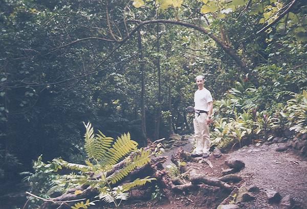 Man in white t-shirt on rocky forest trail among ferns and tropical trees