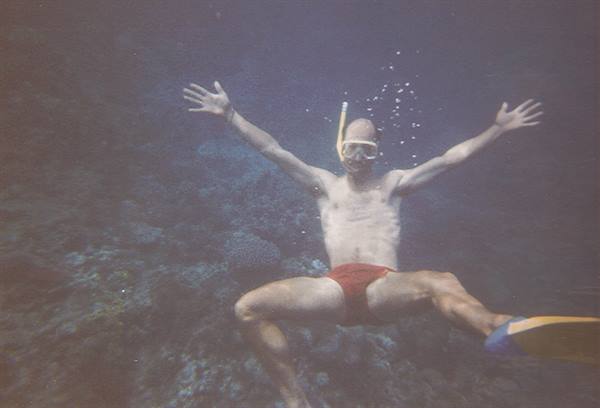 Man with snorkel mask swims underwater over coral reef, arms spread