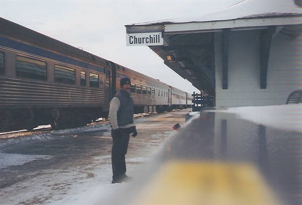 Man on snowy platform beside train, Churchill station sign overhead