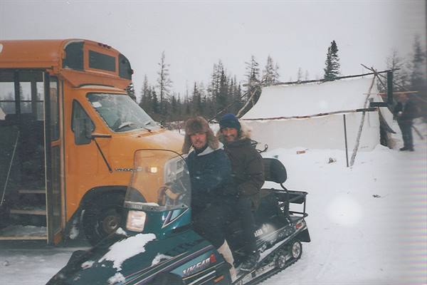 Two men on a Yamaha snowmobile beside a yellow bus in the snow
