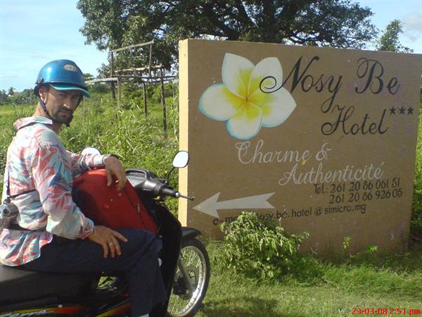 Tourist on a scooter in front of the wooden Nosy Be Hotel sign
