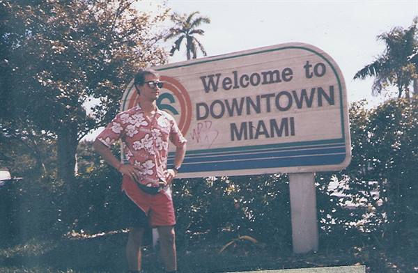Man in floral shirt posing beside the Welcome to Downtown Miami sign