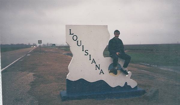Young man sitting on the large white Louisiana roadside sign