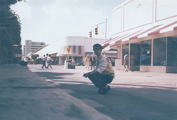 Man crouching on sidewalk in front of shops with striped awnings