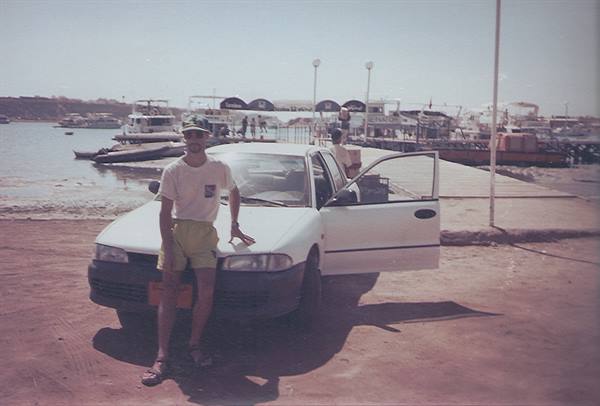 Tourist leaning on a white car in front of Naama Bay harbor