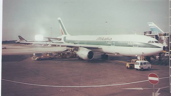 White and green Alitalia airplane parked at the airport among service vehicles