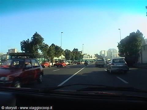 Sunny city avenue with cars in lanes, trees and buildings ahead