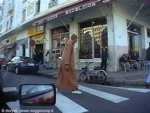 Man in brown djellaba crossing the street in front of Café Excelsior