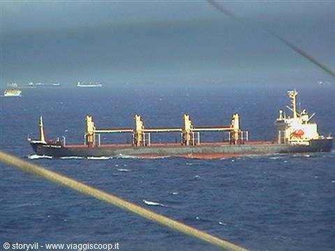 Cargo ship with yellow cranes sailing on open sea under cloudy sky