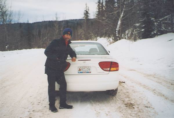 Man in blue hat leaning on a white car on snowy road