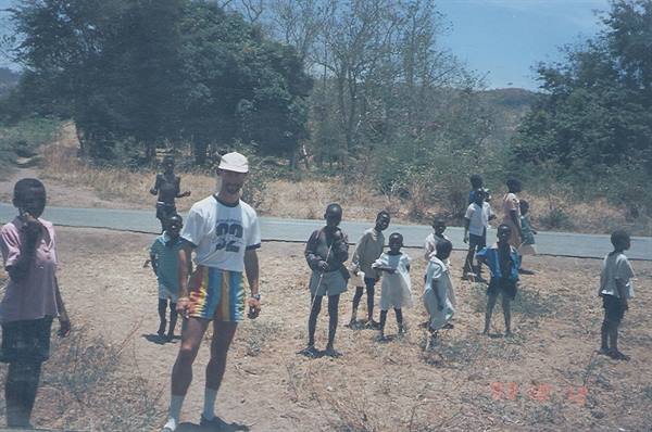 Tourist in colorful shorts with local children by the paved road, bright sun