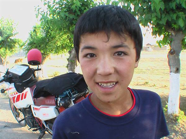 Smiling boy in front of a motorcycle loaded with bags, under trees