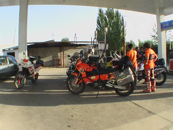 Adventure motorcycles parked under a canopy, two riders in orange suits talking