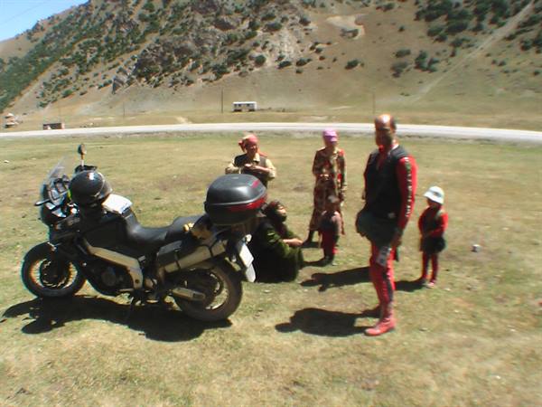 Nomad family with children standing beside a touring motorcycle in mountain meadow