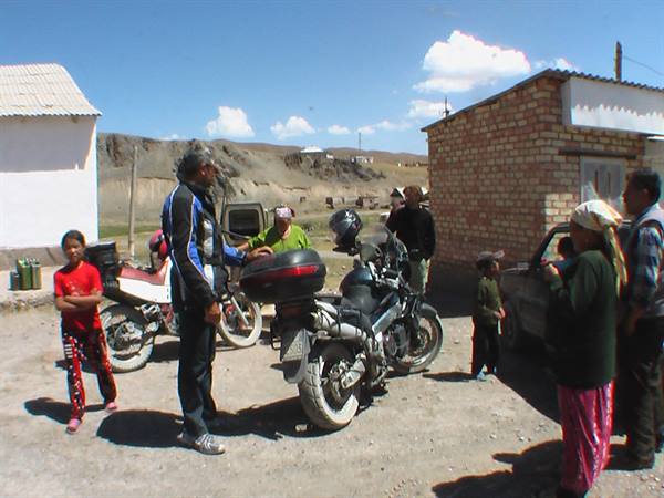 Motorcyclists with touring bikes among villagers, brick houses and arid hills