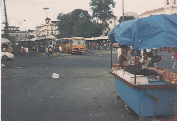 Fruit cart with blue tarp, orange bus and crowds in a city square
