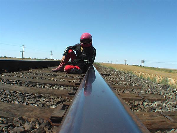 Motorcyclist in pink helmet sitting on a railway rail among wooden ties and gravel