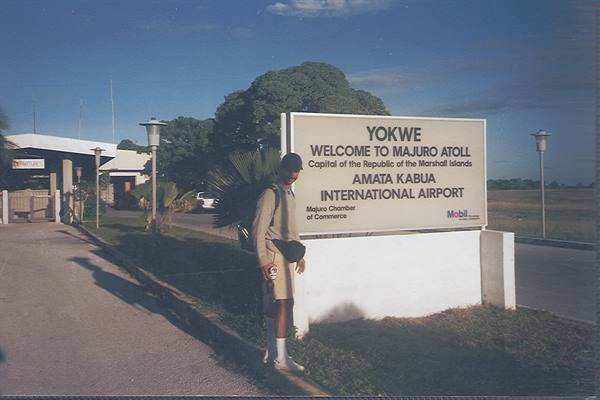 Traveler with backpack beside the white Amata Kabua airport sign at Majuro