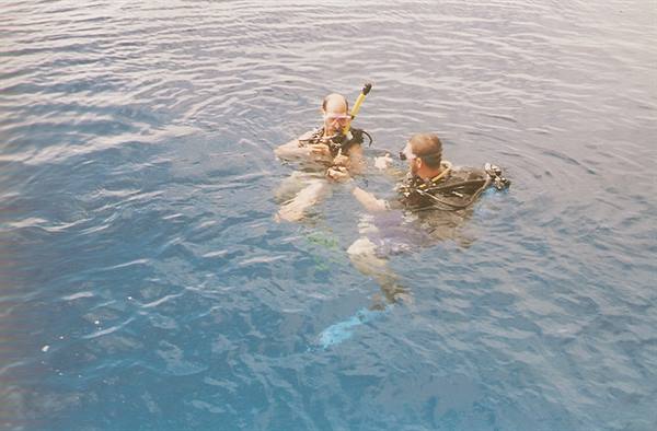 Two scuba divers in full gear preparing to dive in blue sea