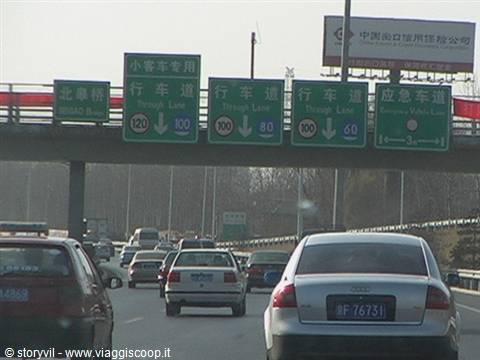 Cars driving on a Chinese highway under green signs showing speed limits