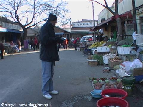 Tourist in black jacket photographing fruit at a Chinese street market