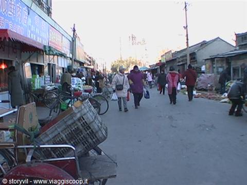 Street market with pedestrians, bicycles and stalls among shops with Chinese signs